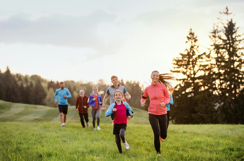 A group of people of all ages running towards the viewer at sunset in a park